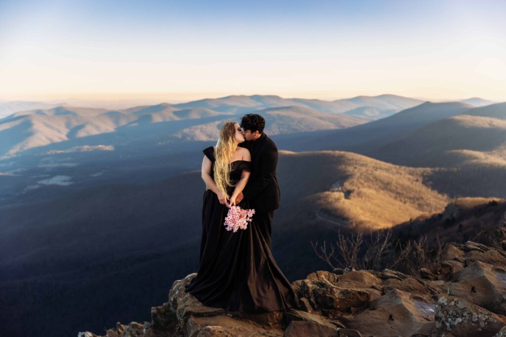 a women in a black dress and a groom in a black suit kiss each other while eloping on a mountain top in Shenandoah National Park