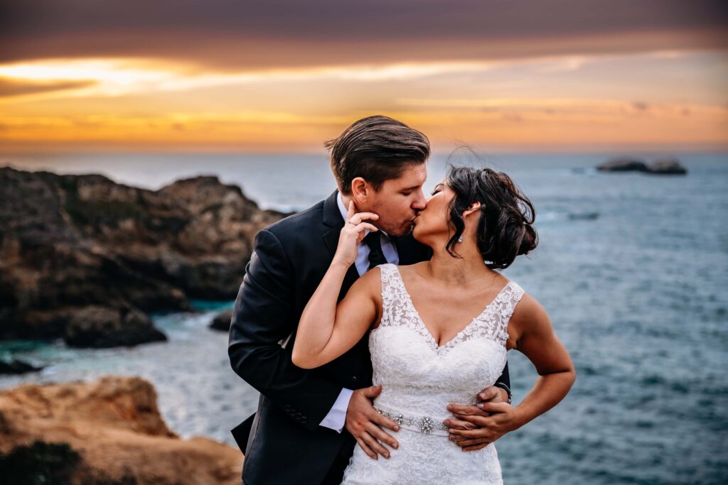 a couple kisses each other with the sun setting behind them during their Big Sur destination elopement