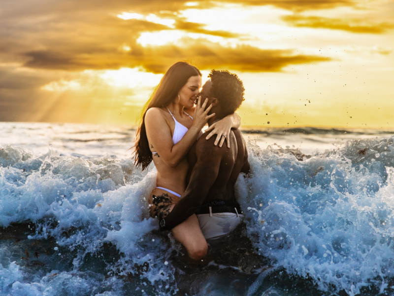 a couple kisses in the ocean as waves crash into them and the sun rises behind them, engagement session guide