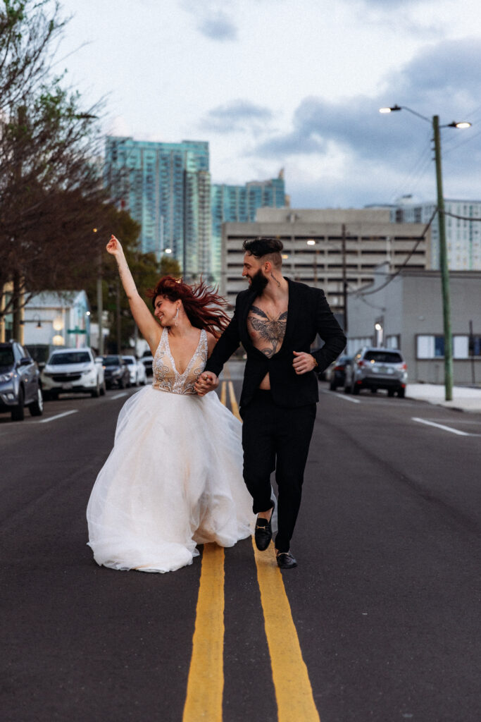 A couple celebrates their Florida elopement near the Tampa Riverwalk, running hand in hand down a city street with joyful energy, captured by Florida Elopement Photographer Shannon Lee.
