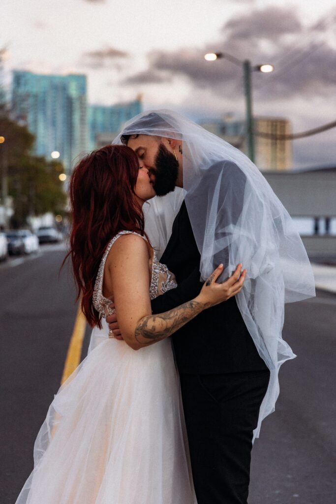 A couple shares a romantic Florida elopement moment in Downtown Tampa, kissing in the middle of a quiet street with city buildings in the background, captured by Florida Elopement Photographer Shannon Lee.