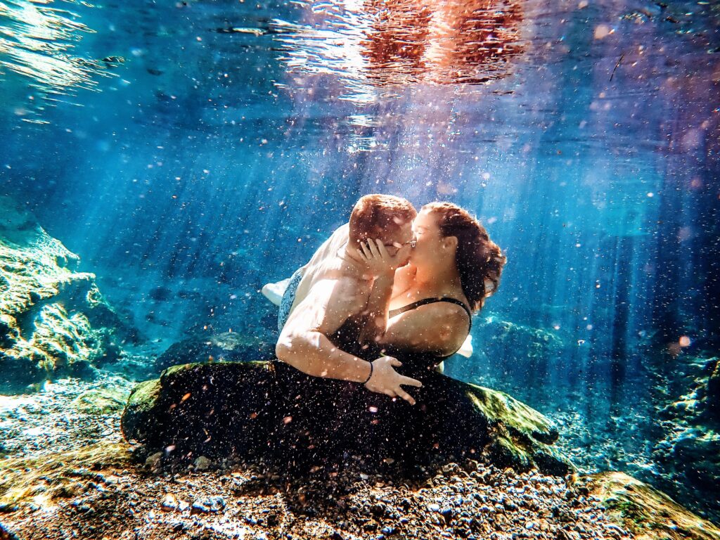A couple eloped in Florida and shares a passionate kiss underwater, surrounded by vibrant rays of light filtering through the water.