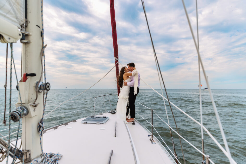 A couple eloped in Florida and shares a romantic kiss on the bow of a sailboat, surrounded by the vast ocean and an open sky.