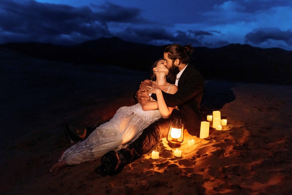 a couple kisses surrounded by a candlelight picnic during their elopement in Great Sand Dunes National Park, Colorado