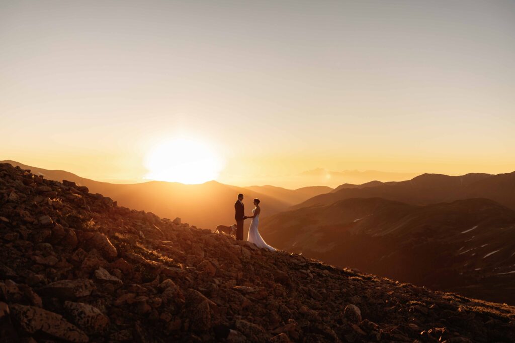 A couple says their vows on a mountain outside of Breckenridge, Colorado for their mountain elopement as the sun rises behind them.