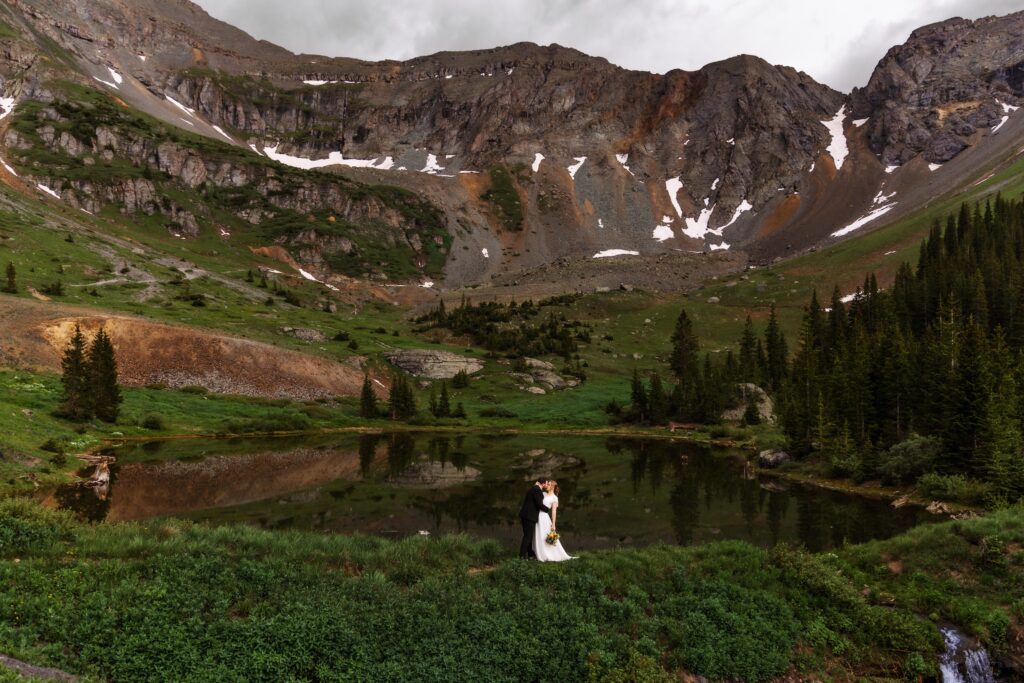 a couple kisses in front of an alpine lake for the San Juans Mountain Elopement in Colorado