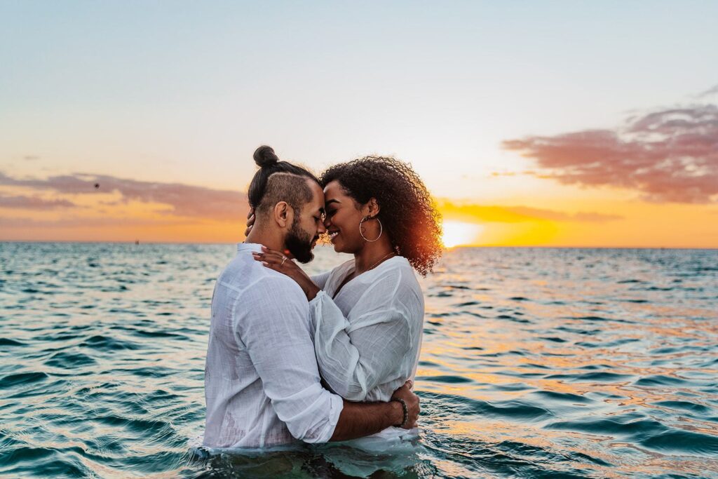 A couple eloped in Florida and shares a tender moment in the ocean at sunset, gazing into each other’s eyes with the sun casting a warm glow behind them.