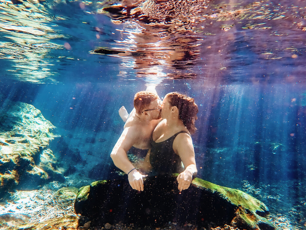 A couple shares an intimate Florida elopement moment underwater in a crystal-clear spring, kissing as sunlight filters through the water, captured by Florida Elopement Photographer Shannon Lee.