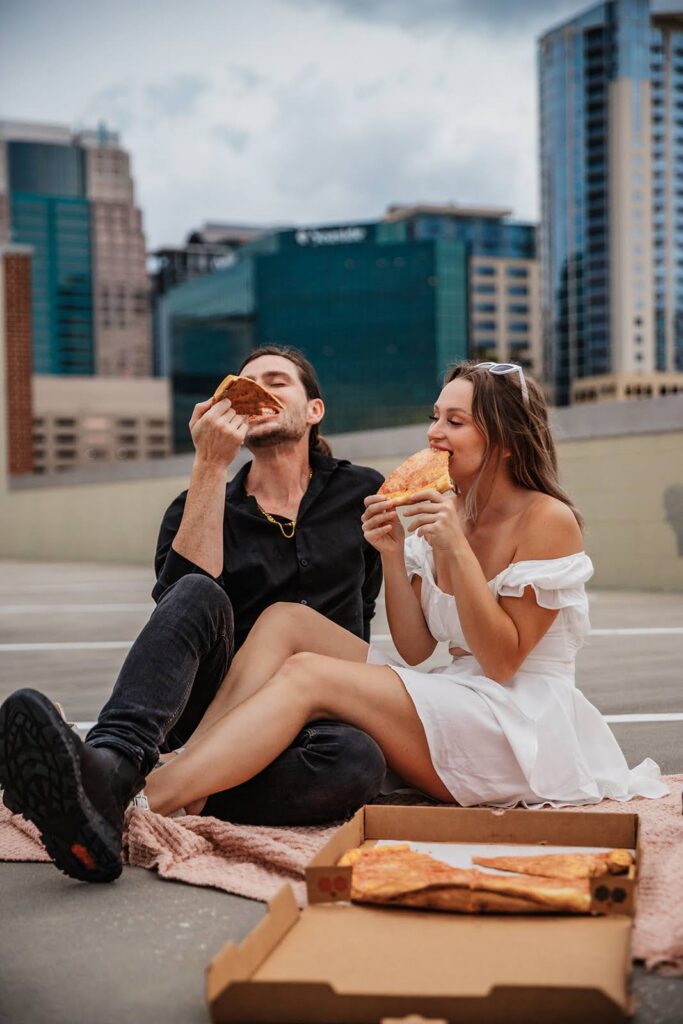 A couple shares a relaxed Florida elopement moment on an Orlando rooftop, sitting together and eating pizza with the city skyline behind them, captured by Florida Elopement Photographer Shannon Lee.