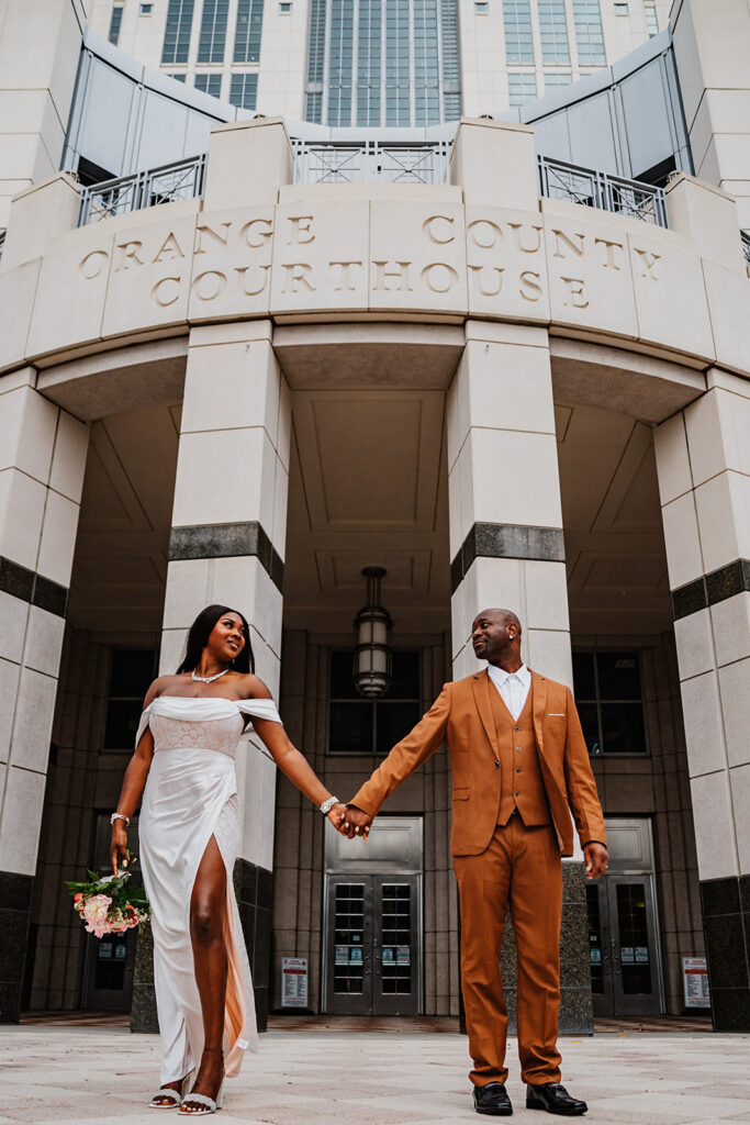 A couple shares a classic Florida elopement moment outside the Orange County Courthouse, holding hands and smiling at each other after their ceremony, captured by Florida Elopement Photographer Shannon Lee.
