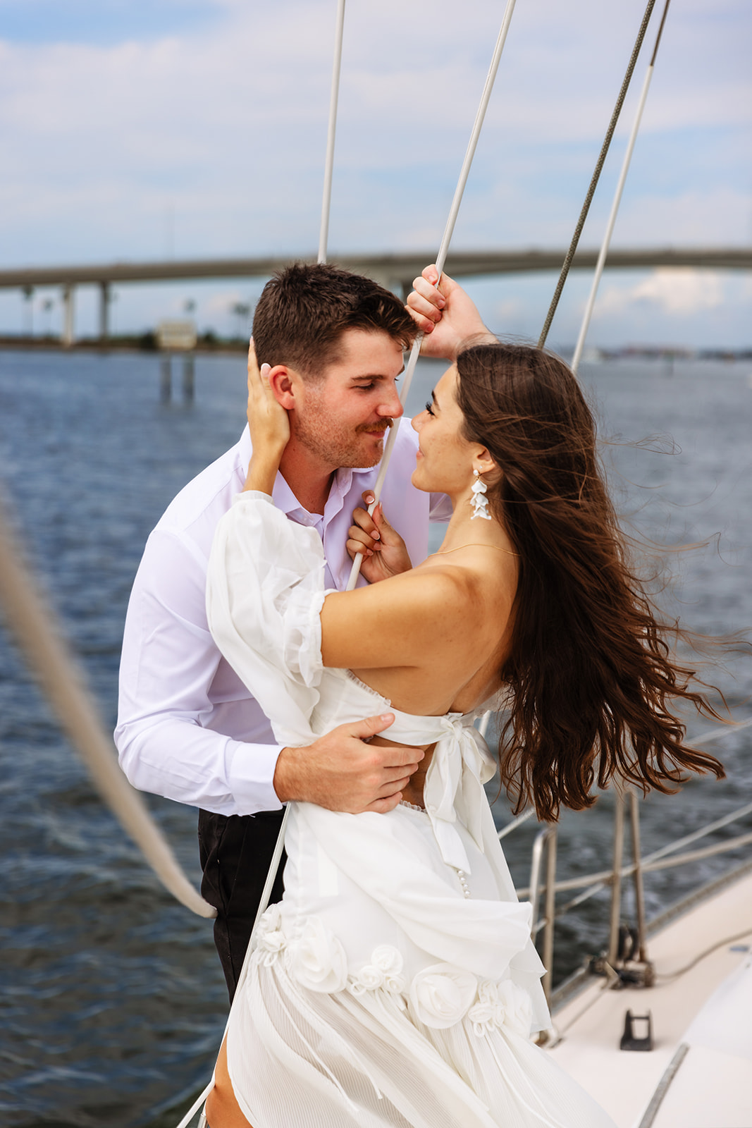 A couple shares a romantic Florida elopement moment aboard a sailboat off the coast, holding each other close as the wind moves through her dress, captured by Florida Elopement Photographer Shannon Lee.