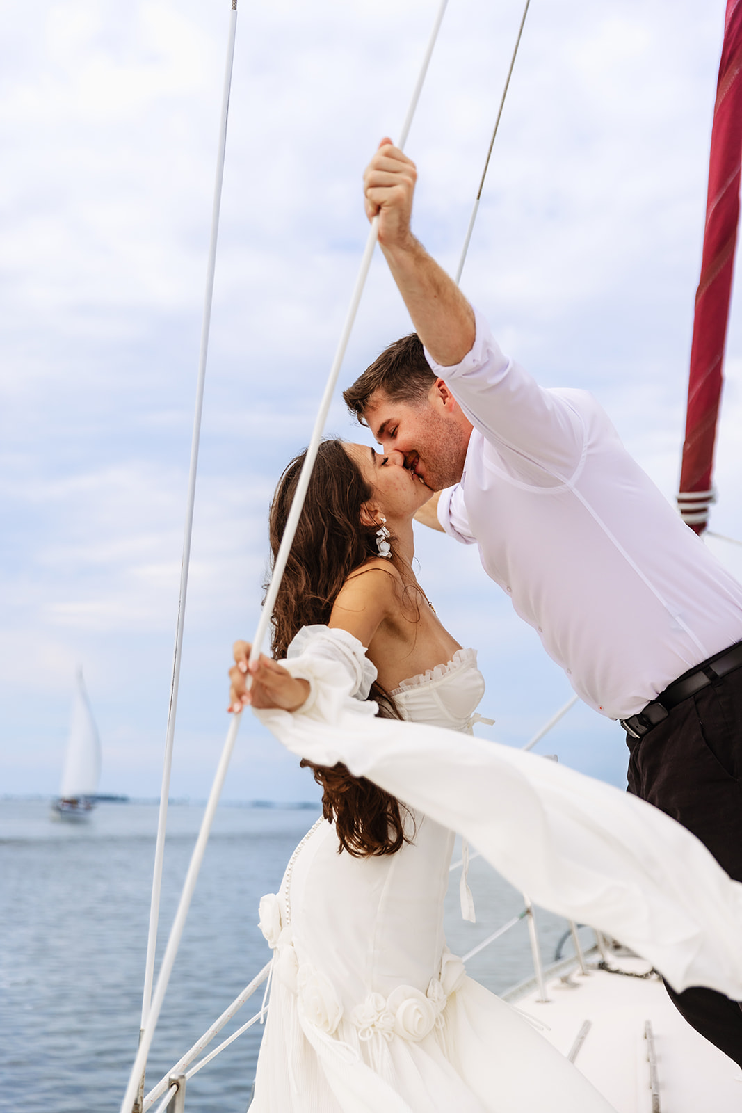 A couple shares a joyful Florida elopement moment aboard a sailboat off the coast, kissing as they lean into each other with the ocean behind them, captured by Florida Elopement Photographer Shannon Lee.