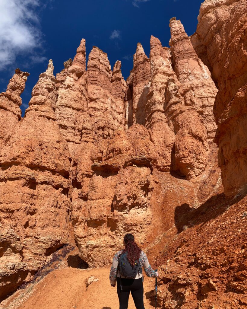 A hiker standing among the towering red hoodoos of Bryce Canyon National Park, a one-of-a-kind national park to elope with dramatic desert formations and stunning views.