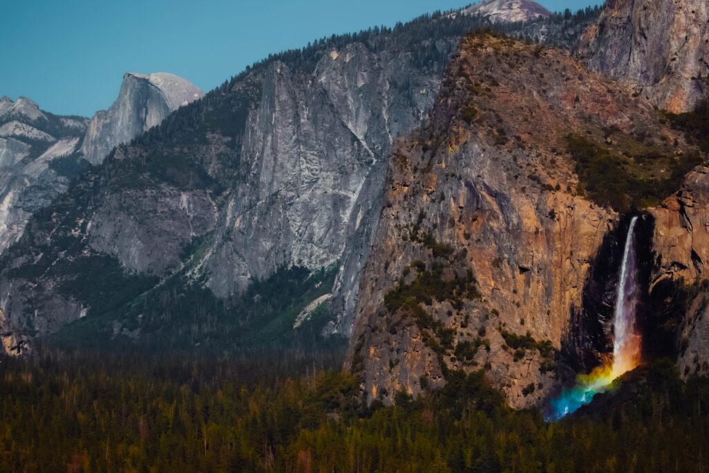 A rainbow glows at the base of a waterfall in Yosemite National Park, one of the most iconic national parks to elope with dramatic granite cliffs and timeless scenery.