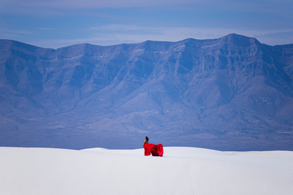 A person in a flowing red dress walking across the bright dunes of White Sands National Park, a unique national park to elope with striking desert beauty and endless horizons.