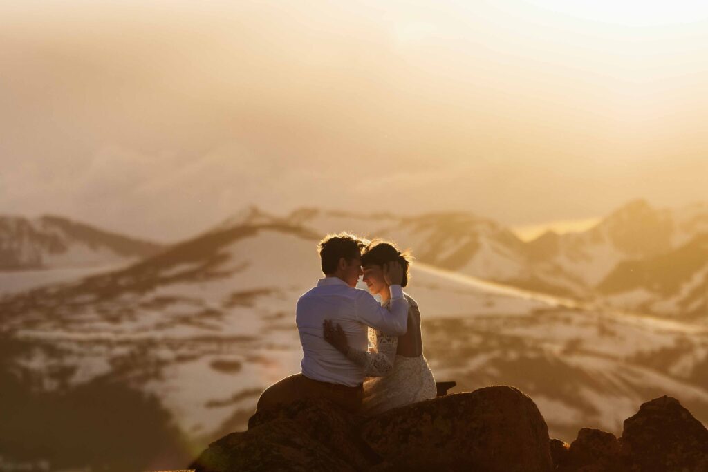 Couple embracing at sunset with snowy peaks in the background of Rocky Mountain National Park, a breathtaking national park to elope for adventurous mountain weddings.