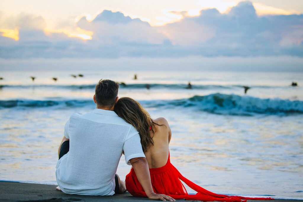 An engaged couple sits together on the shore at Cocoa Beach during sunset, photographed by Orlando Engagement Photographer Shannon Lee.