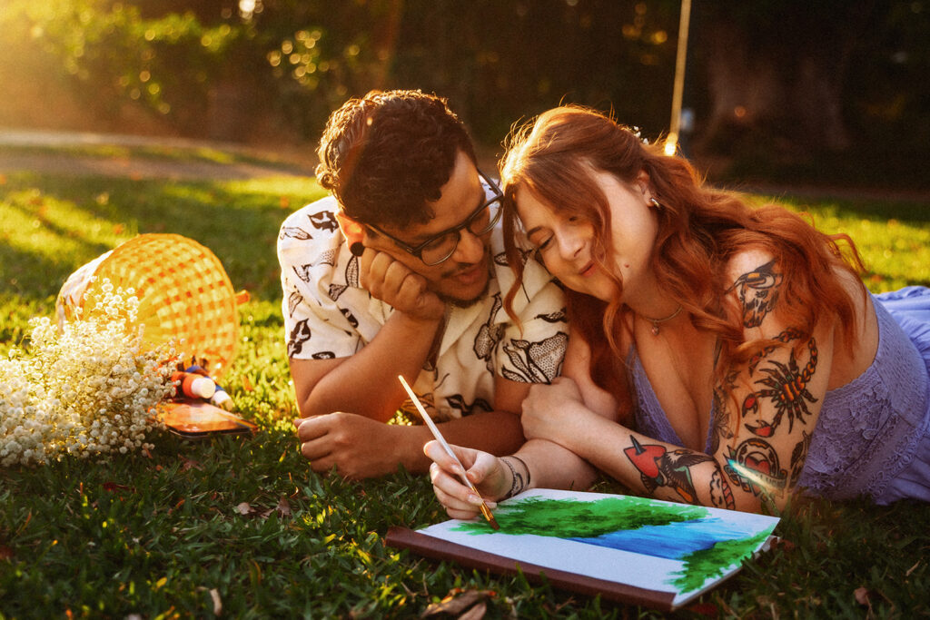 An engaged couple paints together during a picnic at Harry P. Leu Gardens, photographed by Orlando Engagement Photographer Shannon Lee.