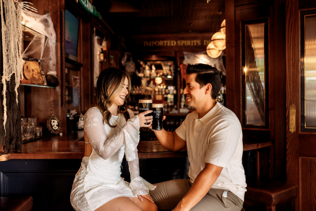 An engaged couple shares a toast with drinks at a cozy brewery, photographed by Orlando Engagement Photographer Shannon Lee.