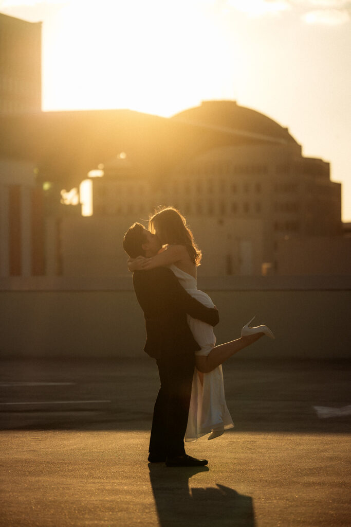 An engaged couple shares a romantic kiss during their golden hour engagement session as the man lifts the woman off the ground, captured by Orlando Engagement Photographer Shannon Lee
