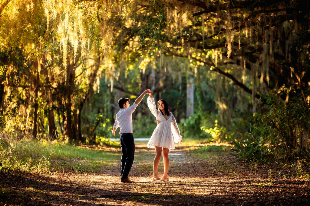 An engaged couple twirls along a sunlit trail beneath oak trees at Lake Louisa State Park, photographed by Orlando Engagement Photographer Shannon Lee.