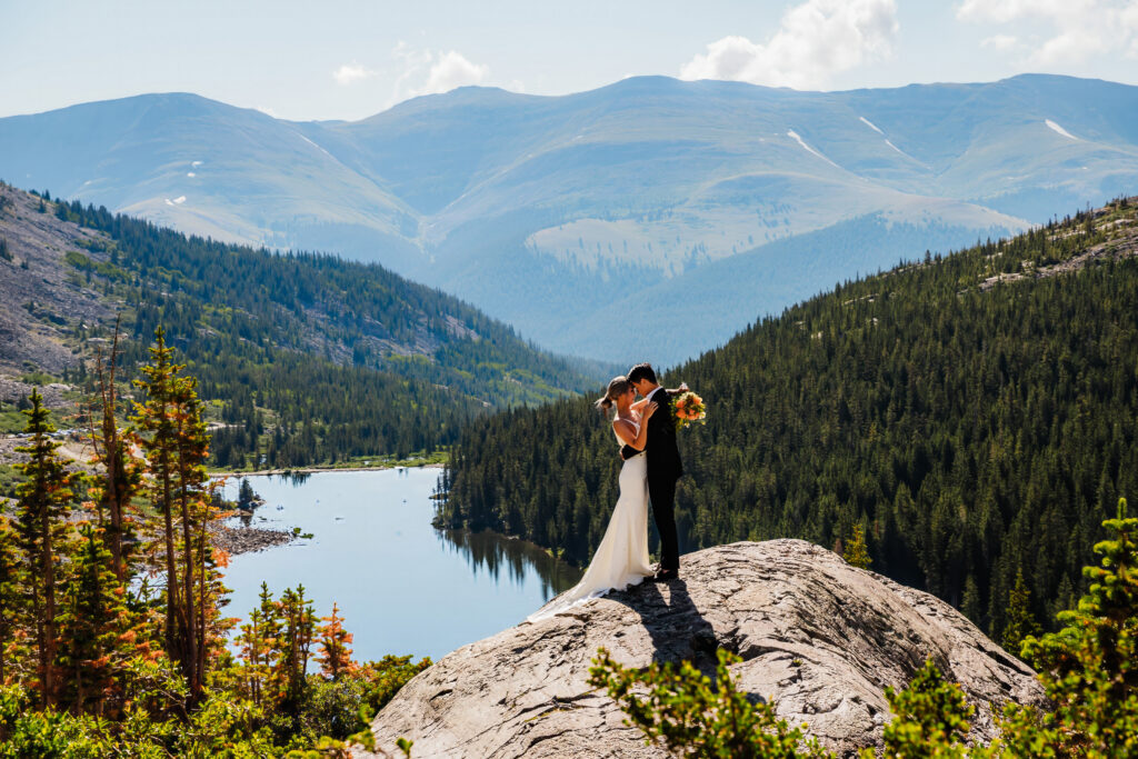 A couple kisses on a rocky outcrop above an alpine lake for their Breckenridge elopement in Colorado.