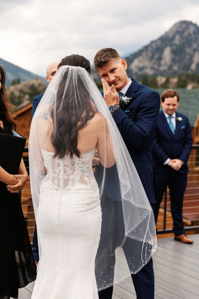 A groom wipes away tears as his bride stands across from him during their ceremony for their Estes Park elopement in Colorado.