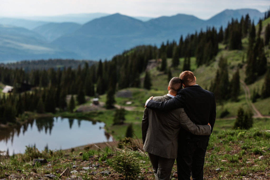 A couple holds each other close as they overlook an alpine lake and rolling peaks for their Telluride elopement in Colorado.