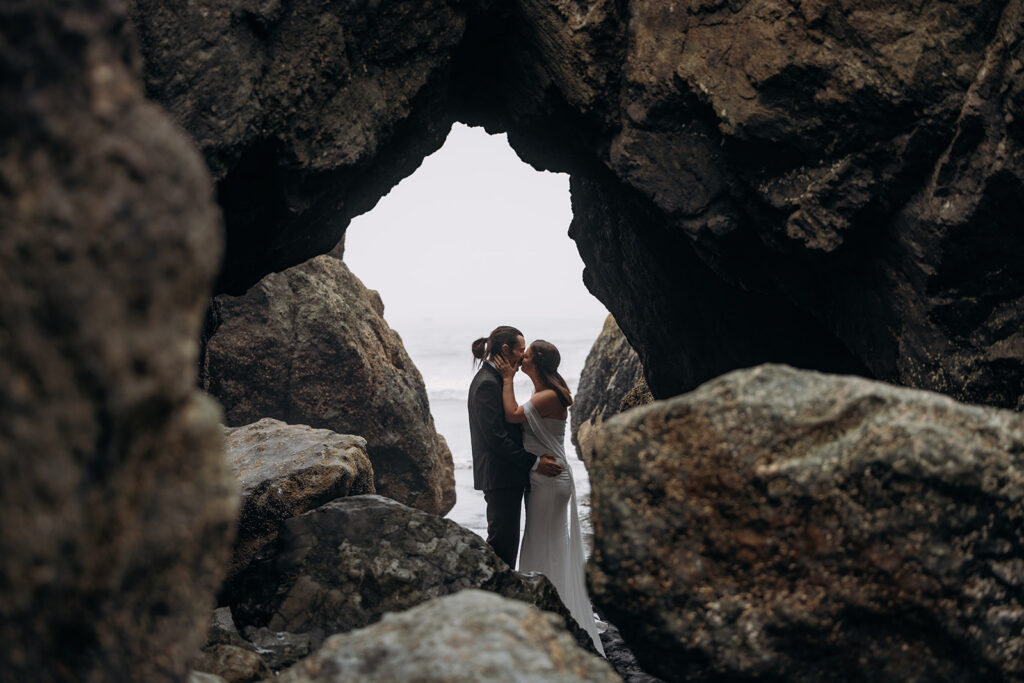 Couple kissing framed by sea stack arch during Ruby Beach Elopement, Olympic National Park, Washington
