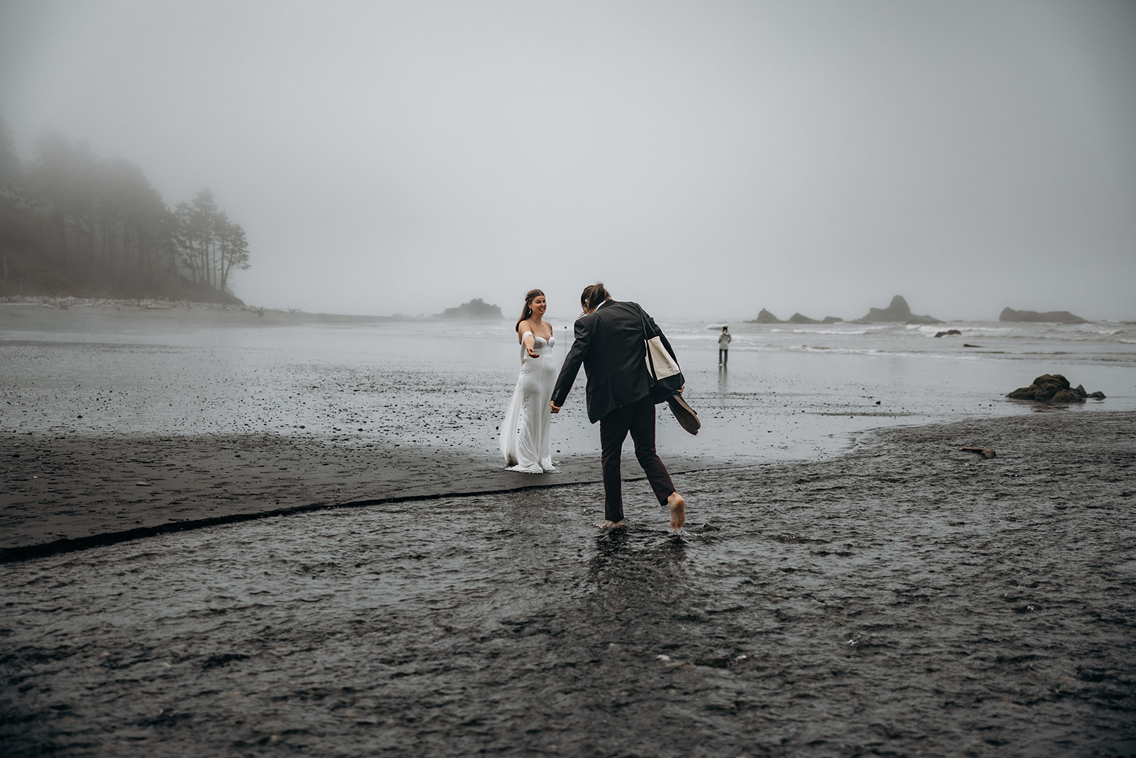 Groom crossing tide pool toward bride during Ruby Beach Elopement, Olympic National Park, Washington