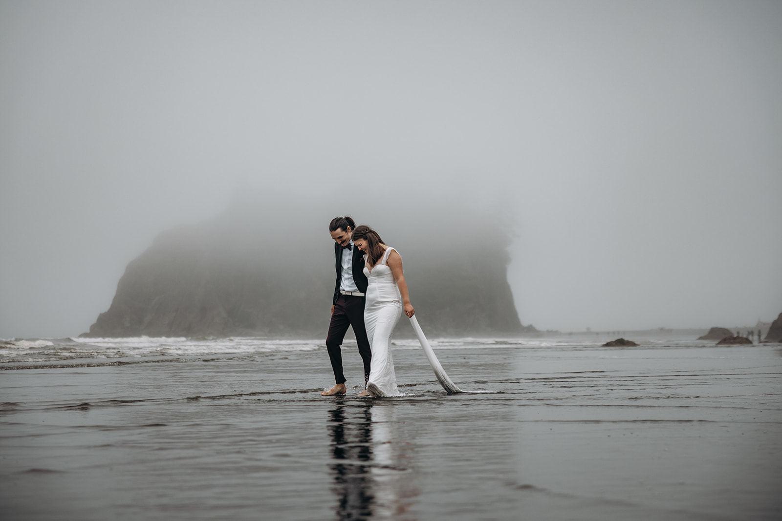 Bride holding train while walking beach during Ruby Beach Elopement, Olympic National Park, Washington