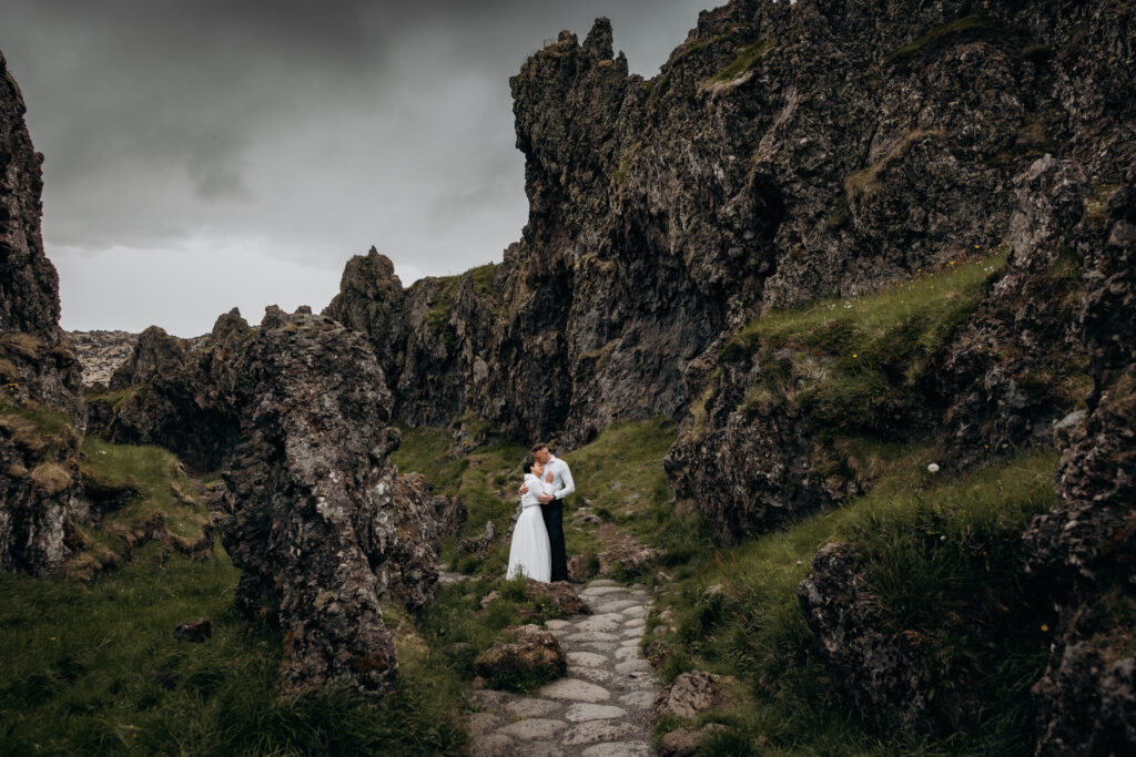 A couple embraces on a stone path nestled between dramatic rocky cliffs during their Iceland elopement, under a moody grey sky.
